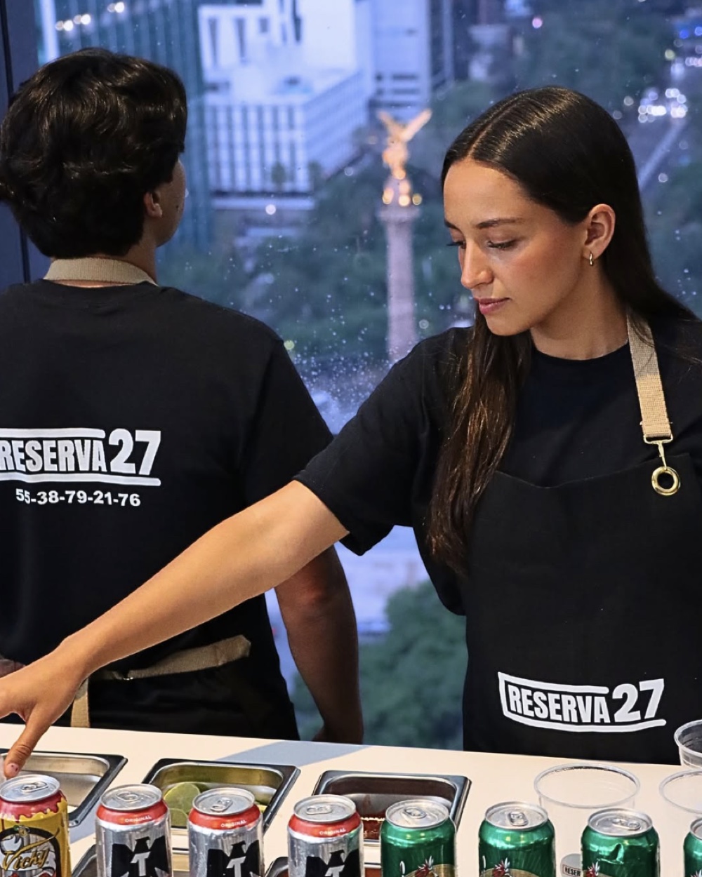 Baristas de Reserva 27 atendiendo la barra de micheladas en un evento en CDMX con vista al Ángel de la Independencia.